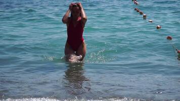 kvinna resa hav. Lycklig kvinna med lång hår i en röd baddräkt och armband i boho stil njuter de vågor på de strand i sommar. förtjusande Lycklig feminin avkopplande på sommar strand på semester. video