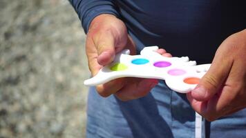 man spelar pop- den fidget leksaker, närbild på händer. oigenkännlig manlig skjuter bubblor på färgrik silikon poppit med fingrar. stänga upp på Flerfärgad anti-stress leksaker. påfrestning lättnad video