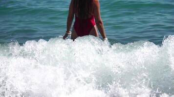 jovem mulher com grandes cabelo dentro uma vermelho roupa de banho e pulseiras dentro boho estilo desfrutando a ondas em a de praia dentro verão. adorável feliz feminino relaxante às verão de praia tendo período de férias. lento movimento. video