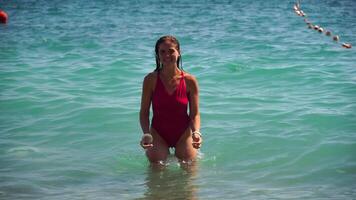 joven mujer con largo pelo en un rojo traje de baño y esposas en boho estilo disfrutando el olas en el playa en verano. adorable contento femenino relajante a verano playa teniendo vacaciones. lento movimiento. video