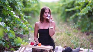 Beautiful woman with long hair drinks white wine from a glass at sunset in the vineyard. A woman's hand shakes a glass of white wine slightly. Wine tasting and wine making concept. Slow motion video