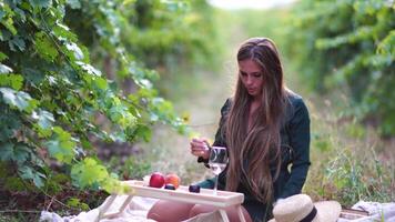 mooi vrouw met lang haar- drankjes wit wijn van een glas Bij zonsondergang in de wijngaard. een vrouw hand- schudt een glas van wit wijn lichtelijk. wijn proeverij en wijn maken concept. langzaam beweging video