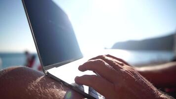 Man laptop sea. Working remotely on seashore. Happy successful man male freelancer working on laptop by the sea at sunset, makes a business transaction online. Freelance, remote work on vacation video