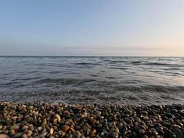 Meer Strand Horizont. Meer Wellen mit weich, schaumig Wasser Waschen mehrfarbig Kieselsteine auf ein Strand während Sonnenuntergang. niemand. Urlaub Erholung Konzept. abstrakt nautisch Sommer- Ozean Sonnenuntergang Natur schleppend Bewegung video