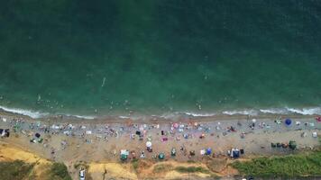 Aerial view of a sandy beach during summer sunset. Crowds of happy people relax by the blue water of the sea bay. Holiday recreation in a natural ocean setting. video