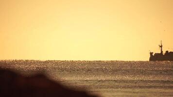 silhouette de pêche navire dans le mer sur horizon. navire voile dans le mer. petit vagues sur le d'or surface de chaud l'eau avec bokeh lumières de le Soleil. mer, la nature et Extérieur Voyage. video