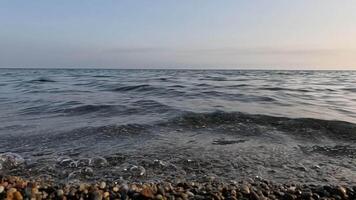 zee strand horizon. zee golven met zacht, schuimend wateren het wassen veelkleurig steentjes Aan een strand gedurende zonsondergang. niemand. vakantie recreatie concept. abstract nautische zomer oceaan zonsondergang natuur langzaam beweging video