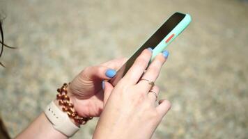 vrouw met smartphone. detailopname van vrouw handen Holding verticaal mobiel telefoon en vegen omhoog vinger toepassing bladzijde tegen achtergrond van zee en strand video