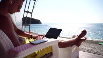 Man laptop sea. Working remotely on seashore. Happy successful man, male freelancer working on laptop on beach, relieves stress from work to restore life balance. Freelance, remote work on vacation video