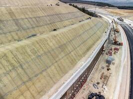 Mountain road constraction. Workers reinforce the slope over the new road. Road construction in progress on slope nature canyon. Infrastructure development and logistics. Aerial drone shot photo