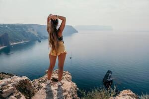 Woman travel sea. Happy tourist enjoy taking picture outdoors for memories. Woman traveler looks at the edge of the cliff on the sea bay of mountains, sharing travel adventure journey photo