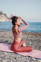 medio Envejecido bien mirando mujer con negro cabello, aptitud instructor en polainas y tapas haciendo extensión y pilates en yoga estera cerca el mar. hembra aptitud yoga rutina concepto. sano estilo de vida foto