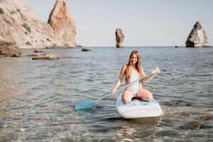 Woman sea sup. Close up portrait of happy young caucasian woman with long hair looking at camera and smiling. Cute woman portrait in a white bikini posing on sup board in the sea photo
