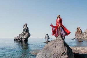 mujer viaje mar. joven contento mujer en un largo rojo vestir posando en un playa cerca el mar en antecedentes de volcánico rocas, me gusta en Islandia, compartiendo viaje aventuras viaje foto