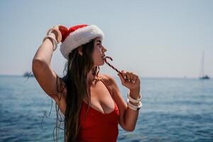Woman travel sea. Happy tourist enjoy taking picture on the beach for memories. Woman traveler in Santa hat looks at camera on the sea bay, sharing travel adventure journey photo