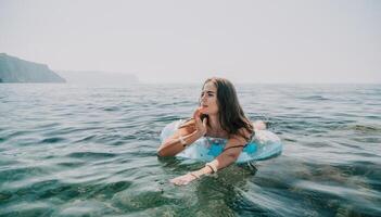 Woman summer sea. Happy woman swimming with inflatable donut on the beach in summer sunny day, surrounded by volcanic mountains. Summer vacation concept. photo