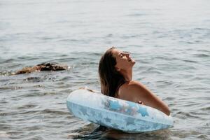 mujer verano mar. contento mujer nadando con inflable rosquilla en el playa en verano soleado día, rodeado por volcánico montañas. verano vacaciones concepto. foto