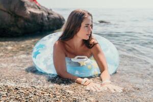 mujer verano mar. contento mujer nadando con inflable rosquilla en el playa en verano soleado día, rodeado por volcánico montañas. verano vacaciones concepto. foto