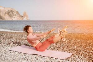 mujer mar pilates deportivo contento medio Envejecido mujer practicando aptitud en playa cerca mar, sonriente activo hembra formación con anillo en yoga estera afuera, disfrutando sano estilo de vida, armonía y meditación foto