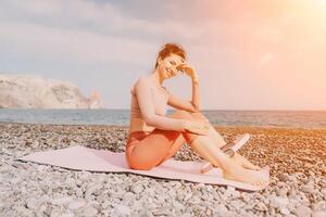 mujer mar pilates deportivo contento medio Envejecido mujer practicando aptitud en playa cerca mar, sonriente activo hembra formación con anillo en yoga estera afuera, disfrutando sano estilo de vida, armonía y meditación foto