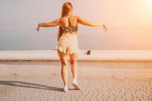 mujer verano bailar. silueta de un contento mujer quien bailes, giros y levanta su manos a el cielo. un juguetón joven mujer disfruta su contento momento bailando en el rayos de el dorado Dom. foto