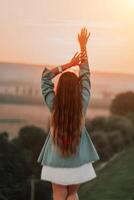 Happy woman standing with her back on the sunset in nature in summer with open hands. Romantic beautiful bride in white boho dress posing with mountains on sunset photo