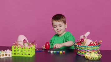 extático pequeño niño utilizando acuarela y pinceles a Decorar huevos y crear festivo cestas como festivo preparativos. contento niño disfruta pintura y colorante decoraciones para Pascua de Resurrección. cámara una. video