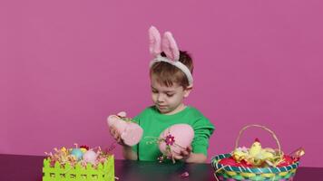 piccolo lieta bambino presentazione nascosto fatto a mano ornamenti creato nel preparazione di Pasqua vacanza celebrazione. giovane ragazzo con coniglietto orecchie mostrando dipinto decorazioni, un' coniglio e un uovo. telecamera un. video