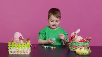 Little cheerful boy crafting handmade easter decorations by painting with watercolor and paintbrushes. Small young kid using art supplies coloring eggs for holiday, decorating activity. Camera A. video