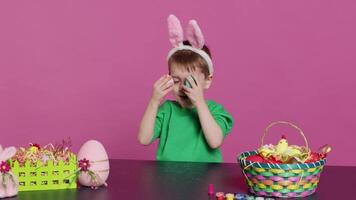 Smiling cute kid playing peek a boo game with painted colorful eggs, having fun with easter decorations and arrangements on camera. Enthusiastic joyful boy being excited about holiday. Camera A. video