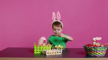 content petit enfant organiser des œufs et poussin dans une panier dans préparation pour Pâques dimanche célébrations, création de fête décorations dans studio. peu garçon ayant amusement coloration. caméra b. video