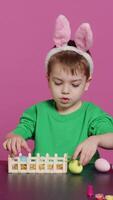 Vertical Video Happy toddler with bunny ears arranging basket filled with painted eggs, creating festive arrangements for the easter sunday celebration. Cheerful little kid enjoys art and craft. Camera A.