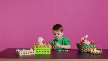 en extase peu enfant en utilisant aquarelle et pinceaux à décorer des œufs et créer de fête paniers comme de fête dispositions. content enfant jouit La peinture et coloration décorations pour Pâques. caméra b. video