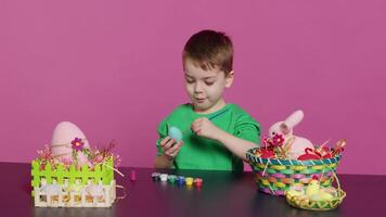 Joyful small kid painting eggs for easter holiday festivity in studio, using watercolor and art supplies. Smiling preschooler coloring festive ornaments in preparation for sunday. Camera A. video