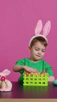 Sweet young boy making colorful arrangements for Easter holiday festivity, putting painted eggs in a handcrafted basket. Ecstatic joyful kid using crafting materials to create decorations. Camera B. video