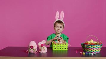 Excited little kid decorating baskets with eggs and grass to prepare for easter holiday festivity, creating festive arrangements. Cute toddler with bunny ears does craft activity. Camera B. video