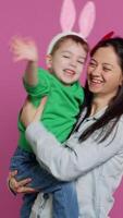 Vertical Video Mother lifting up her little boy and kissing him in studio, showing love and hugging cute kid against pink background. Sweet mom and son embracing each other and laughing. Camera A.