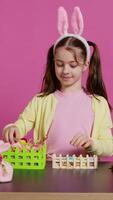 Smiling happy schoolgirl presenting a handmade decorated basket in studio, making easter holiday preparations against pink background. Young child showing handcrafted arrangements. Camera B. video