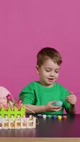 Little cheerful boy crafting handmade easter decorations by painting with watercolor and paintbrushes. Small young kid using art supplies coloring eggs for holiday, decorating activity. Camera B. video