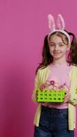 Smiling pleased girl presenting her handcrafted easter basket filled with painted eggs and other festive decorations for holiday celebration. Joyful small kid proud of her arrangement. Camera B. video