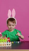 förtjusande liten unge skapar handgjord ornament för påsk söndag och målning ägg med frimärken och borstar. nöjd ung pojke använder sig av konst material till Färg och dekorera. kamera b. video