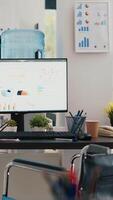 vertikal video rullstol i inklusive kontor för anställda och visas som visar marknadsföring statistik. medicinsk stol i arbetsyta erbjudande tillgänglighet till arbetare med handikapp och monitorer med diagram grafer
