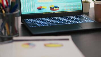 Financial report on desk next to laptop showing marketing statistics in empty office, close up shot. Company files containing business pie charts near notebook left open in workspace video