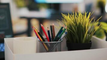 Focus on desk belongings in modern office with notebook in blurry background showing business diagram and figures, close up. Pencil holder, mini house plant, empty coffee mug and graphs on laptop video