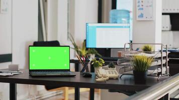 Office with green screen laptop and display in background with scheduled clients list. Mockup notebook in workspace and customers financial consultations list in the back on monitor video