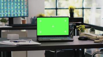 Focus on isolated screen laptop on company desk with computer desktop in blurry background showing stock exchange data. Chroma key notebook and trading platform displayed on PC screen in the back video