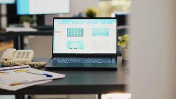 Stock market diagrams with charts and stock figures on laptop sitting on desk in empty workplace. Trading index listings displayed on notebook screen in financial department, panning shot video