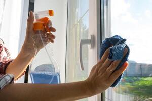 Woman manually washes the window of the house with a rag with spray cleaner and mop inside the interior with white curtains. Restoring order and cleanliness in the spring, cleaning servise photo