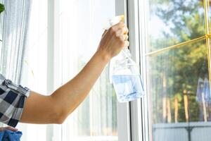 mujer a mano lavados el ventana de el casa con un trapo con rociar limpiador y fregona dentro el interior con blanco cortinas restaurar orden y limpieza en el primavera, limpieza servise foto