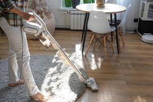 un mujer aspiradoras un redondo alfombra en un casa entre casa plantas con un mano vacío limpiador. general limpieza de el casa, limpieza Servicio y ama de casa foto